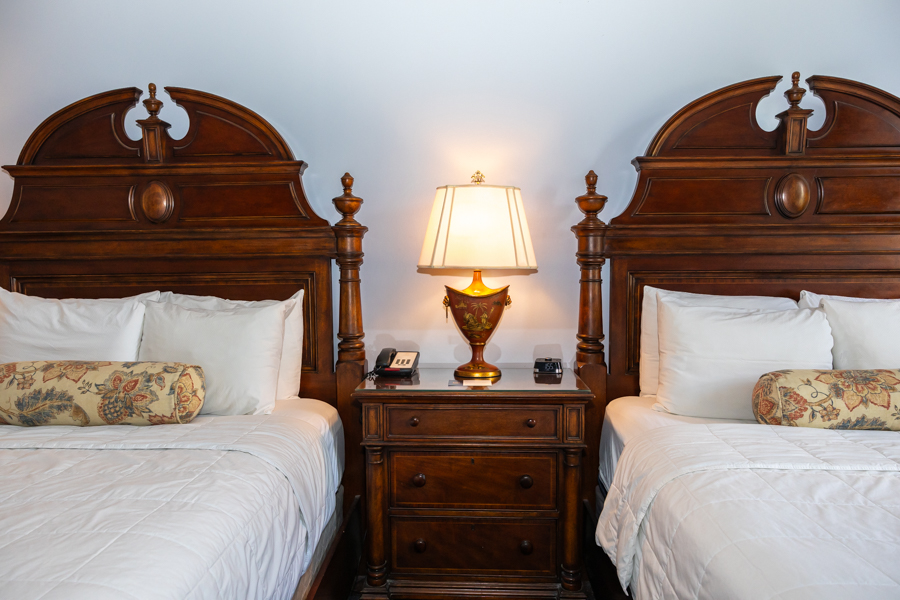 two beds with white pillows and a lamp on a nightstand
